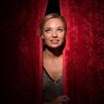 Girl taking a peak out of the red stage curtains