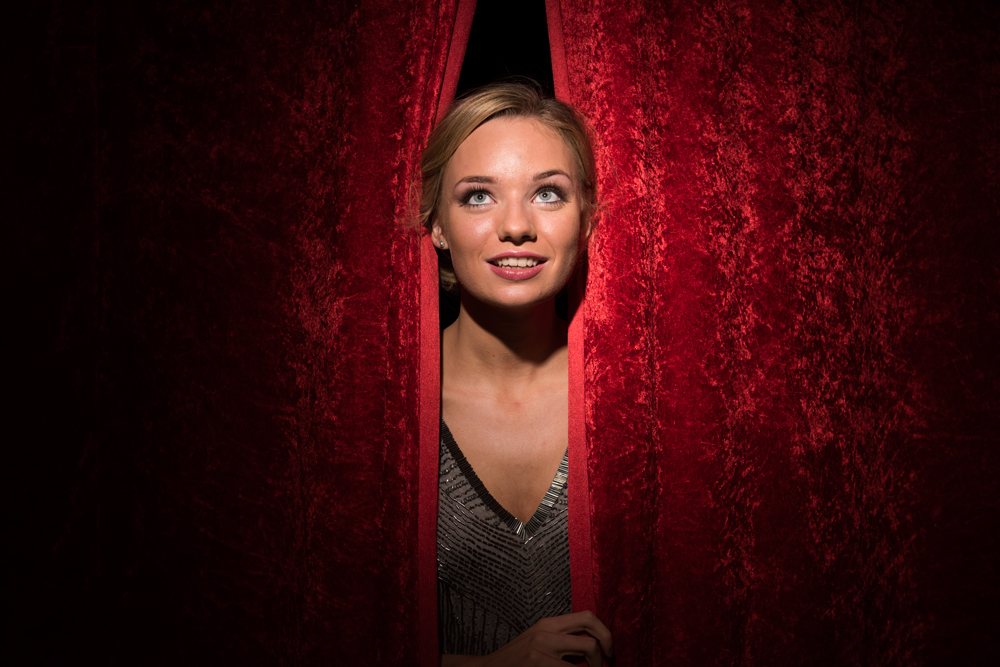 Girl taking a peak out of the red stage curtains