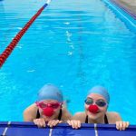 2 students in a swimming pool with red noses on