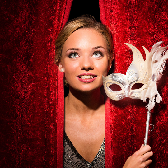 A girl holding a mask behind a curtain